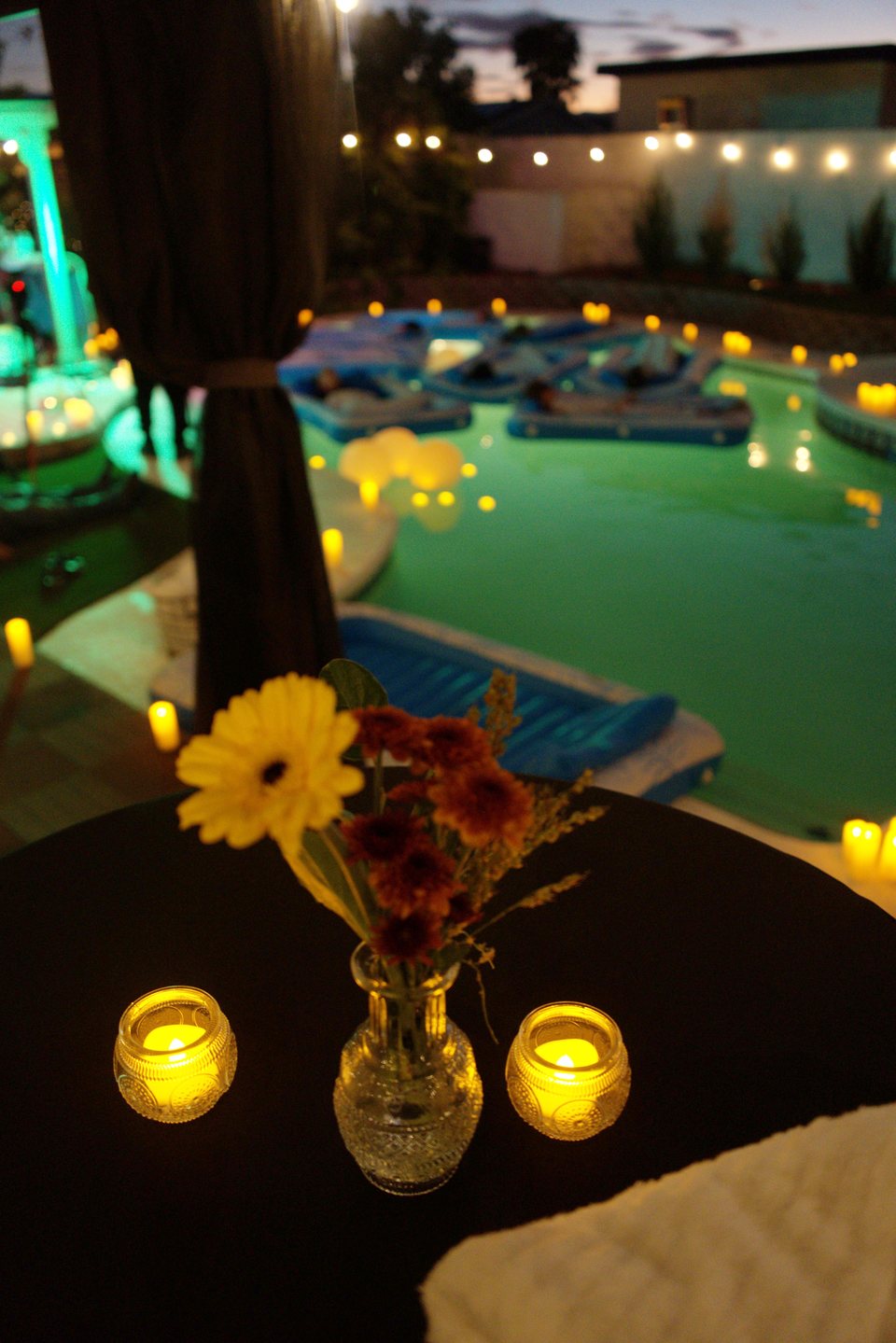 Flowers and candles beside the pool, with guests resting on floaters at the October 18, 2026 gathering