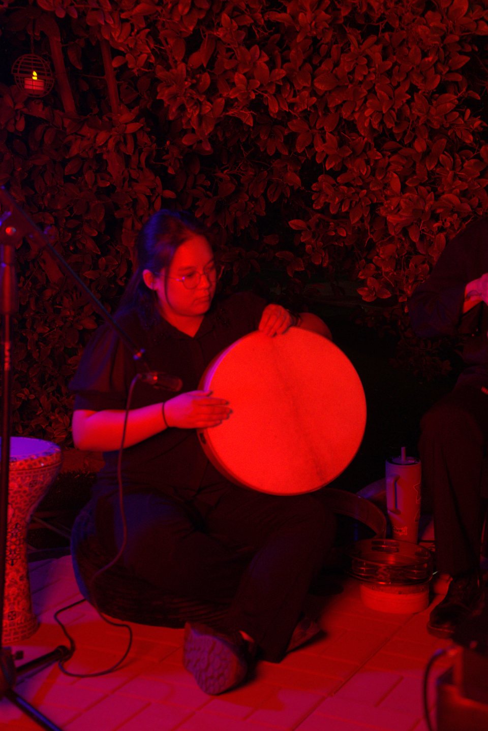 A musician playing a frame drum under red stage lighting